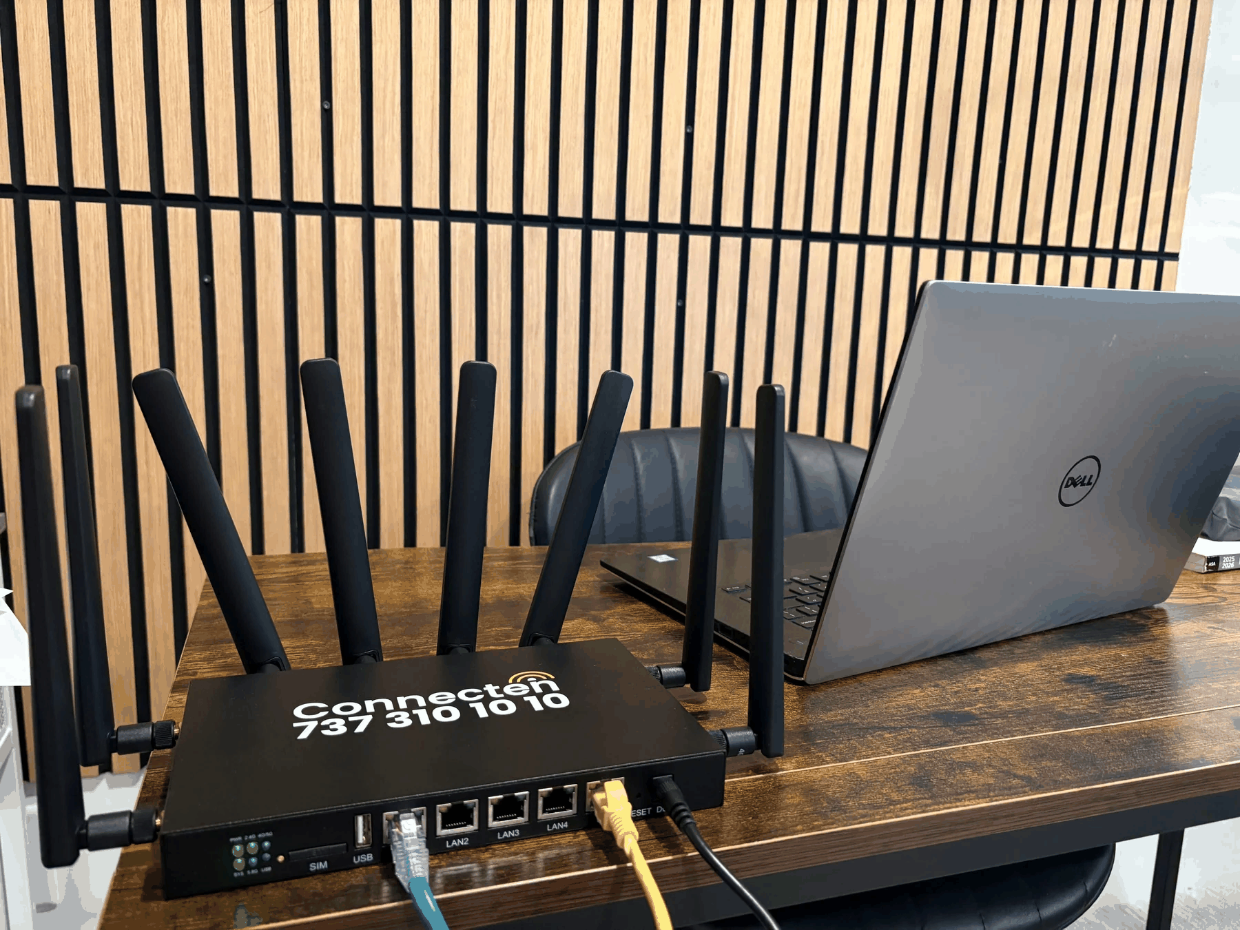 Connecten router on office desk beside Dell laptop with wood slat wall background